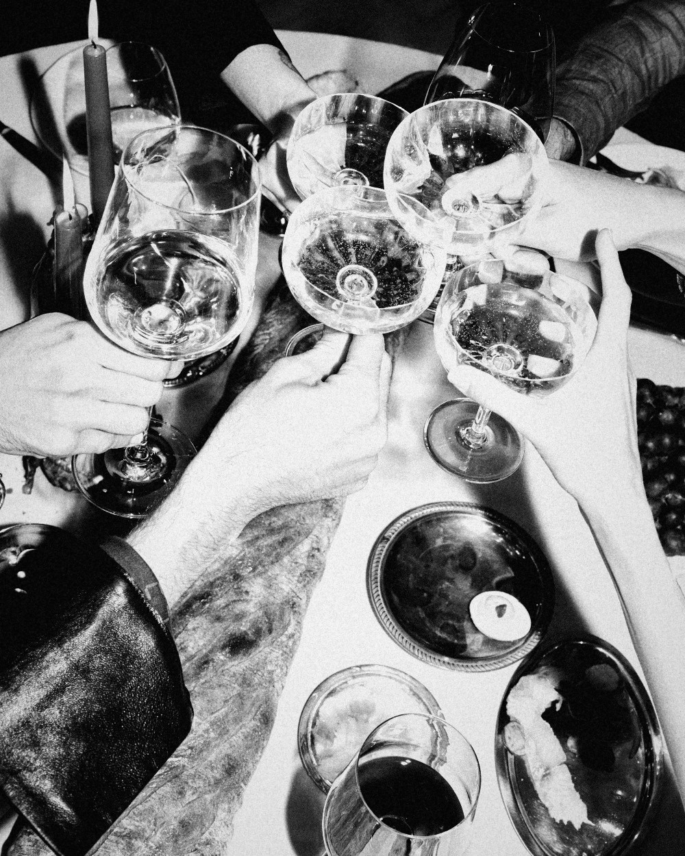 Hands raising wine glasses in a toast over a candlelit table, black and white