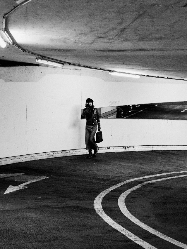 A woman walking alone through a curved concrete parking garage, black and white